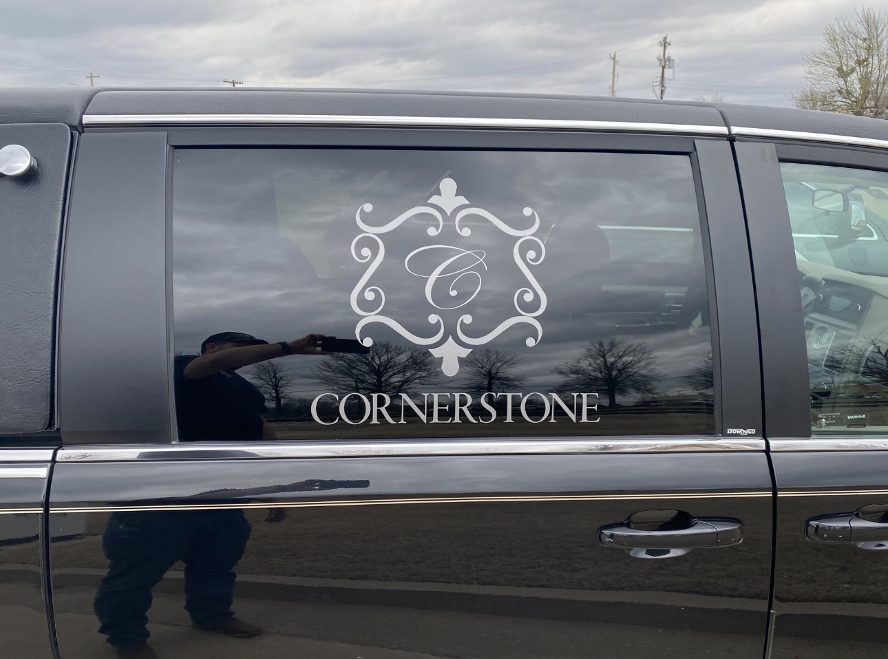 White Cornerstone lettering and decorative monogram applied to the side window of a black vehicle